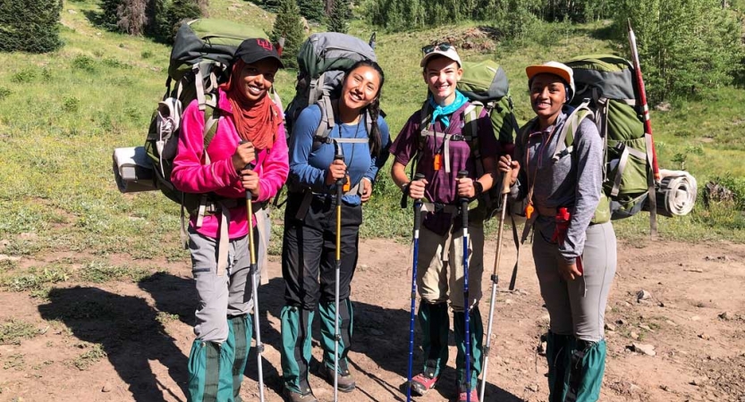 four outward bound students wearing backpacks smile at the camera